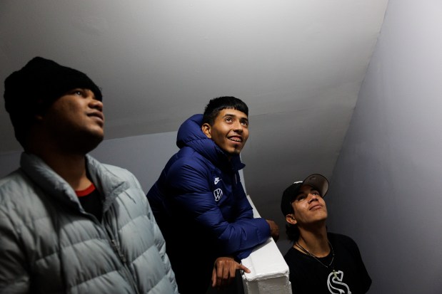 Robinson Covis, 25, from left, Abel Gonzalez, 27, and Daniel Antonio Ruiz, 21, all from Venezuela, watch property manager Chris Amatore install a smoke detector inside a home shared by several migrant families on Jan. 29, 2024. (Armando L. Sanchez/Chicago Tribune)