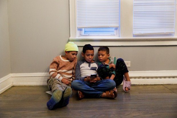 Jeremy Hernandez, 10, from left, Jose Manuel Rodriguez, 10, and Rauly Otero, 6, all from Venezuela, look at a phone inside the home they share with other migrants on Jan. 29, 2024, in Chicago. (Armando L. Sanchez/Chicago Tribune)