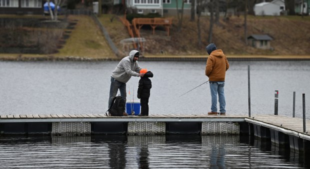 On the pier, John King of Antioch arranges headwear on son Jaxson King, 6, a first-grader. On right is Zac Hebeda, also of Antioch on Feb. 10, 2024 at the 64th annual Ice Fishing Derby in Antioch at Turtle Beach Marina (42273 N. Woodbine Ave.) on Channel Lake.