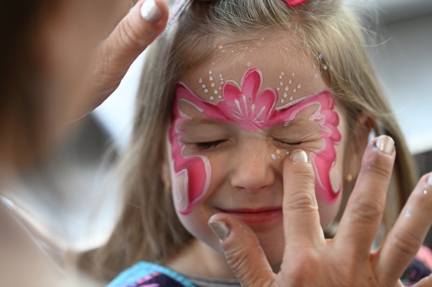 Margot Tennant, 5, a kindergartner from Glencoe, is literally tickled to have glitter applied to her face painting design by makeup artist Diane Hardy of Des Plaines during Subzero Shenanigans at the Weinberg Family Recreation Center on Feb. 19, 2024 in Glencoe. Karie Angell Luc for Pioneer Press