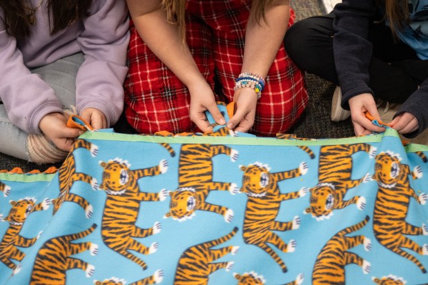 Three Joan Martin Elementary fifth-graders tie tassles around the edge of a blanket into knots with fellow "Brickie Leaders" as they make blankets for Project Linus on Monday, February 12, 2024. (Kyle Telechan for the Post-Tribune)