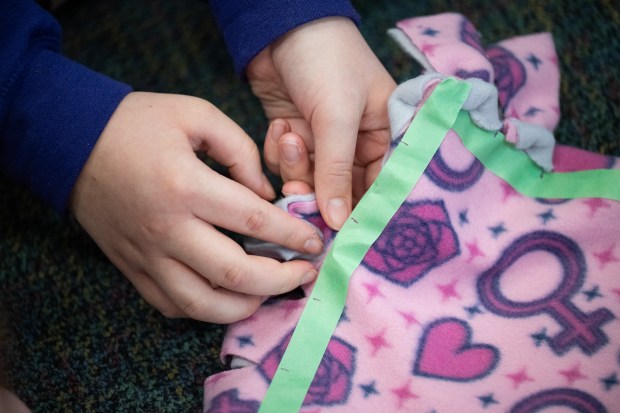 A Joan Martin Elementary fifth-grader ties tassels around the edge of a blanket into knots with her fellow "Brickie Leaders" as they make blankets for Project Linus on Monday, February 12, 2024. (Kyle Telechan for the Post-Tribune)