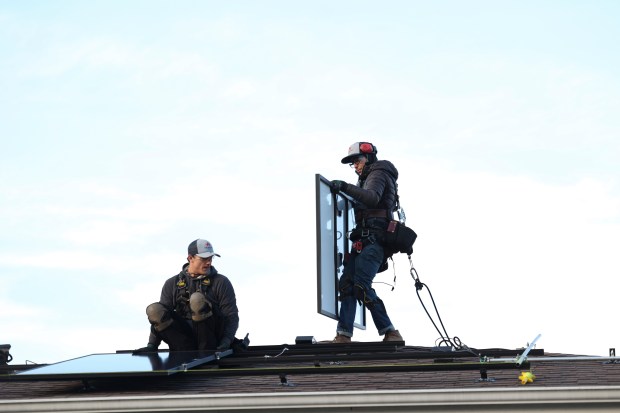 Jared Salvatore (left) prepares a bracket for installation as Garrison Riegel (right), of Celestar Solar, positions a solar panel onto a roof in Schaumburg on Thursday, Nov. 30, 2023. (Trent Sprague/Chicago Tribune)