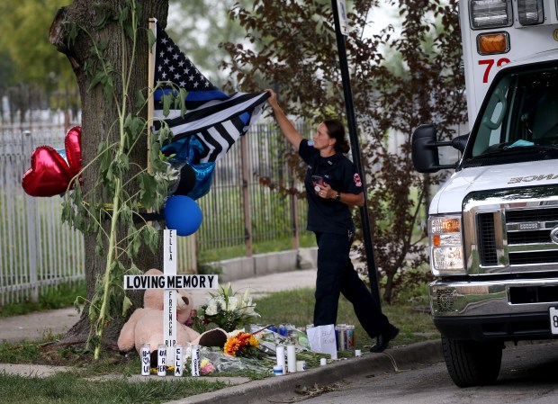 A Chicago Fire Department paramedic unfurals a flag at a memorial for Chicago police Officer Ella French in the 6300 block of South Bell Avenue, Aug. 10, 2021. (Antonio Perez/ Chicago Tribune)