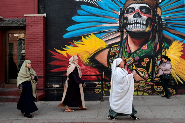 Women walk past a mural as they take part in the Good Friday Via Crucis procession in Chicago's Pilsen neighborhood on March 29, 2024. (Antonio Perez/Chicago Tribune)