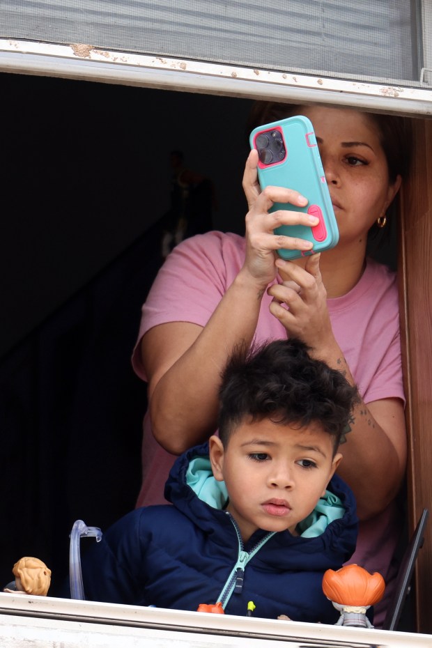 A woman a child look out their window as hundreds of people walk past during the Good Friday Via Crucis procession in Chicago's Pilsen neighborhood on March 29, 2024. (Antonio Perez/Chicago Tribune)