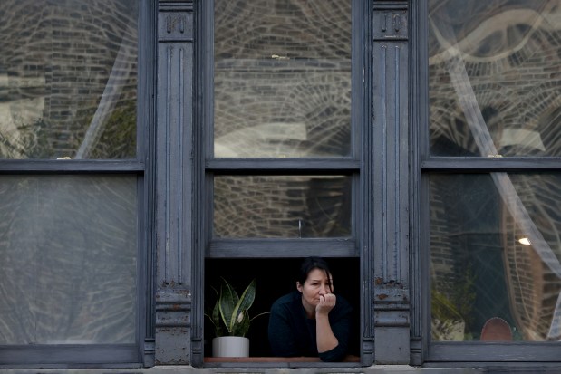 A woman looks out her window as hundreds of people walk during the Good Friday Via Crucis procession in Chicago's Pilsen neighborhood on March 29, 2024. (Antonio Perez/Chicago Tribune)