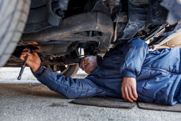 Jonathan Torreyes, 33, from Venezuela, works under a Ford Fusion outside a migrant shelter on North Elston Avenue, March 11, 2024, in Chicago. (Armando L. Sanchez/Chicago Tribune)