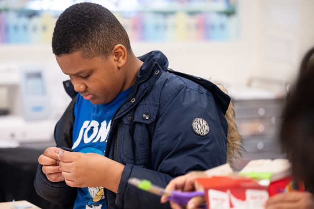 Gary resident Aubrien Higgins-Crosby, 11, cuts a piece of tape as he and others fashion an eclipse-viewer out of cereal boxes during a program at the Gary Public Library on Saturday, March 23, 2024. (Kyle Telechan/for the Post-Tribune)