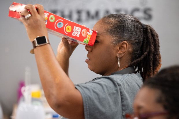 Gary Public Library head of technology Pamela May peers through a cereal box fashioned into an eclipse-viewing device during a program at the Gary Public Library on Saturday, March 23, 2024. (Kyle Telechan/for the Post-Tribune)