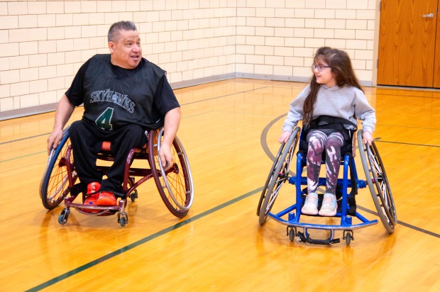 Jorge Alfaro of the Chicago Skyhawks wheelchair basketball team, left, races nine-year-old Nora Ahmed of Valparaiso during an author reading and wheelchair basketball demonstration on Saturday, March 16, 2024 at Thomas Jefferson Middle School in Valparaiso. (Michael Gard/for the Post-Tribune)