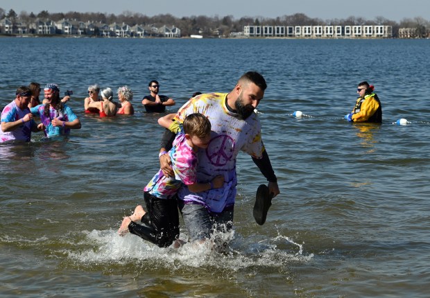 Josh Johnston, of Antioch, carries a shoe and Easton Metzger, 8, on March 2, 2024 at Breezewald Beach in Lake Zurich for the "Purple Plunge" fundraiser for families of cancer patients. (Karie Angell Luc/Pioneer Press)