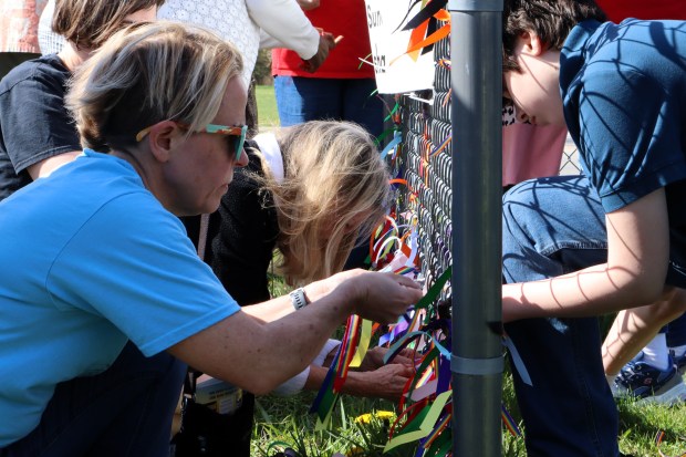 Members from the congregations of HOPE United Church of Christ and Bethany United Methodist Church, along with officials from the city of Aurora, met on Sunday morning to tie rainbow ribbons, which replaced a pride flag that was vandalized, onto HOPE's sign. (R. Christian Smith / The Beacon-News)