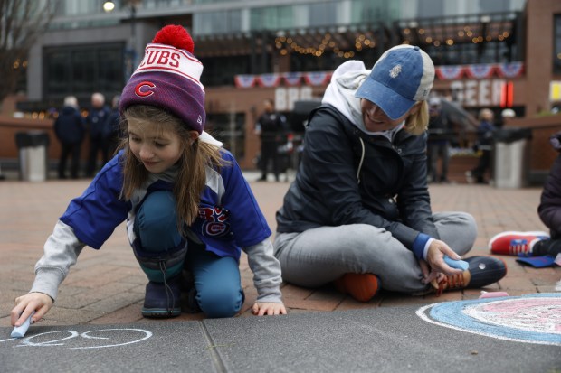 Audrey Hendriksen, 9, draws with chalk next to her mother Suzy Hendriksen outside Wrigley Field ahead of the Chicago Cubs home opener against the Colorado Rockies on April 1, 2024. (Vincent Alban/Chicago Tribune)