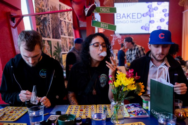 Akemi Almeida, center, smokes a marijuana joint, while Lucas Ewing, left, prepares to smoke marijuana and Brendan Striego, right, smokes a marijuana joint during baked bingo night at OKAY Cannabis Dispensary and West Town Bakery in Wheeling on April 9, 2024. (Vincent Alban/Chicago Tribune)