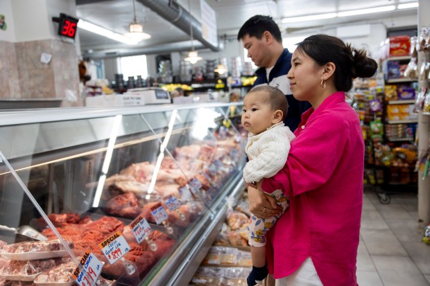 Aiperi Adylbek Kyzy, holds her 9-month-old son, Aikol Toichubekova, while waiting to place an order at the butcher counter on April 20, 2024, at Farm City Meat Halal & Grocers in Chicago. (Vincent Alban/Chicago Tribune)