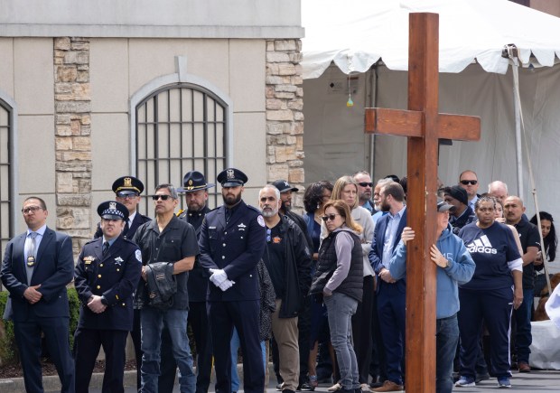 A man holds a large cross while police officers and members of the public line up to enter the visitation for Chicago police Officer Luis M. Huesca on April 28, 2024, at Blake and Lamb Funeral Home in Oak Lawn. Huesca, a CPD officer for six years, was returning home last week after a shift in the CPD's Calumet District when he was fatally shot. (Brian Cassella/Chicago Tribune)