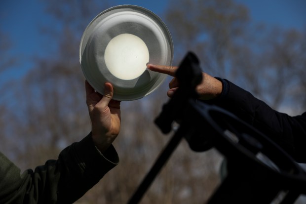 WGN-TV meteorologist Tom Skilling, right, points out a sun spot on a projection of the sun as CJ Dugan, a producer at WGN, holds a paper plate up to his reflector telescope at Dugan's friend's campsite at Little Grassy Lake Campground in Makanda on April 7, 2024. Dugan and his family witnessed the 2017 eclipse with Skilling. (Eileen T. Meslar/Chicago Tribune)