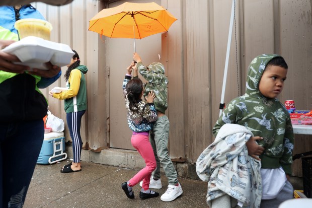 Two children play with an umbrella as their mother, Alejandra Hernandez, left, carries containers of food outside a migrant shelter in the 2200 block of South Halsted Street on Thursday, April 4, 2024, in Chicago. (John J. Kim/Chicago Tribune)