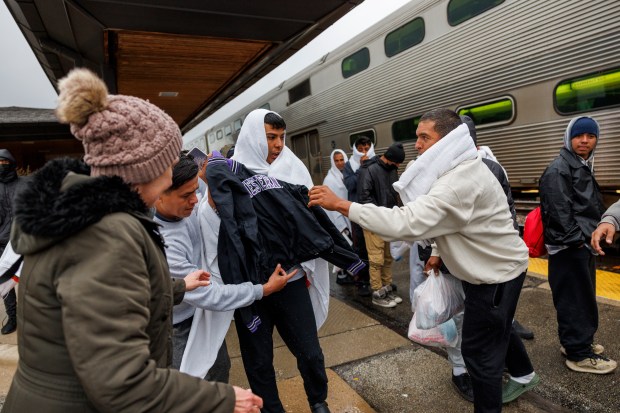 Wendy Fessler, 60, hands out clothing to migrants as they board a Metra train to Chicago after traveling by bus from El Paso, Texas Wednesday, April 3, 2024, in Wilmette. Migrants on the bus said the ride took almost 30 hours. (Armando L. Sanchez/Chicago Tribune)
