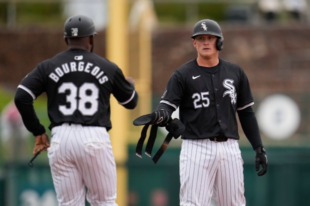 Chicago White Sox's Andrew Vaughn (25) hands over his batting guards to White Sox first base coach Jason Bourgeois (38) during the third inning of a spring training baseball game against the Chicago Cubs Friday, March 15, 2024, in Phoenix. (AP Photo/Ross D. Franklin)