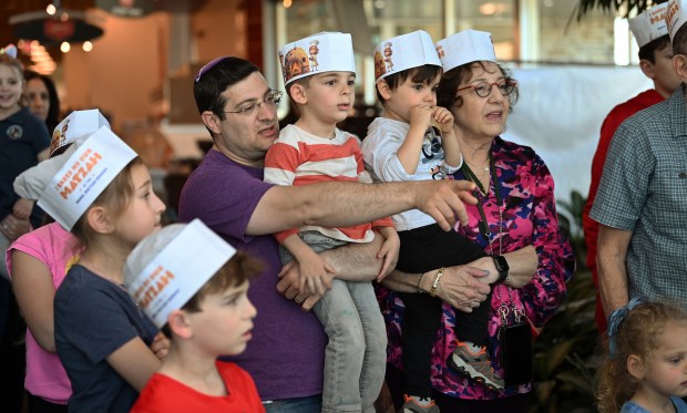 From left to right, (right arm pointed and extended) Mendy Zimmerman of Skokie, holding child Elan Zimmerman, 4, and Jeremy Coleman, 3, of Riverwoods, with Jeremy's grandmother Judy Farah of Northbrook, watch the presentation at the Model Matzah Bakery, a family matzah bake by Chabad of Northbrook at Mariano's in Northbrook on April 15, 2024. (Karie Angell Luc/Pioneer Press)