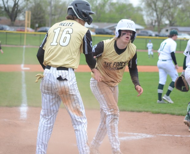 Oak Forest's Ryan Heitz (16) helps Sean Sullivan after both scored on Justin Gibbs' single against Evergreen Park in a South Suburban Conference crossover game in Oak Forest on Thursday, April 18, 2024. (Jeff Vorva / Daily Southtown)