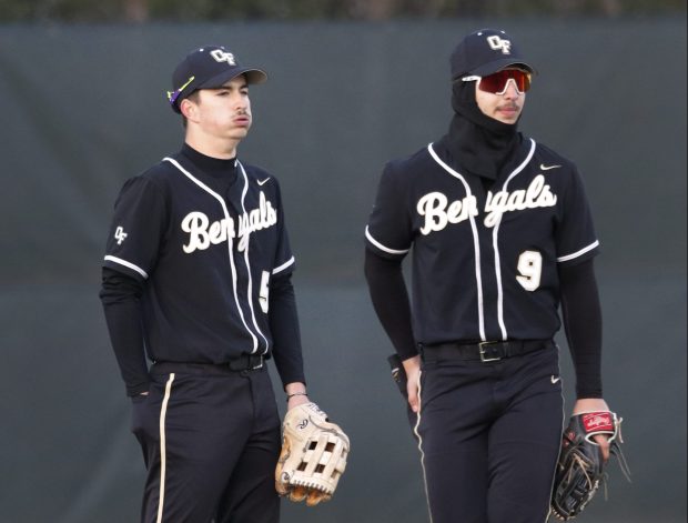 Oak Forest's Evan Gamboa (left) stands with his brother Mateo Gamboa (right) trying to keep warm as they wait for a pitcher change during a baseball game against Homewood-Flossmoor on Wednesday, April 24, 2024. (John Smierciak/for the Daily Southtown)