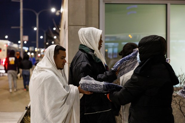 Jordin Benitez, 29, of Venezuela, from left, is given a blanket after walking with other migrants to the city's landing zone after traveling from Glen Ellyn to Ogilvie Transportation Center in the early morning hours of Jan. 5, 2024 in Chicago. (Armando L. Sanchez/Chicago Tribune)