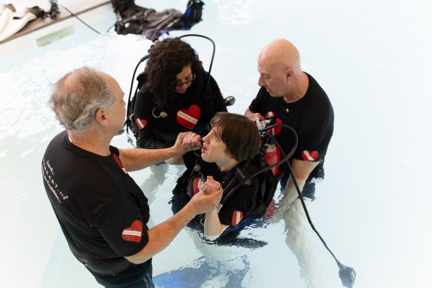 Dive Heart President Jim Elliott and Executive Director Tinamarie Hernandez, help Erin Tunison get her scuba gear on as her father Mike helps her stand during a class in Downers Grove on Monday, April 1, 2024. (Troy Stolt/for the Lake County News Sun)