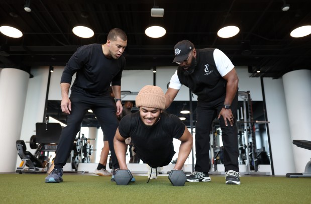 Athletes They Fear founder Kofi Hughes, left, and board member Eddie Sanders place 45-pound weights on the back of Simeon junior Chris Burgess Jr. as he does pushups on April 10, 2024, in Chicago. Burgess is a four-star recruit who's committed to Notre Dame. (John J. Kim/Chicago Tribune)