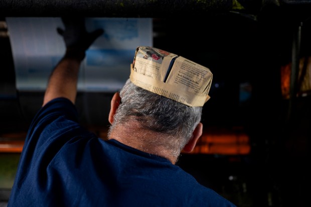 Rick Ramirez, a night shift press operator wearing a newspaper hat, attaches plates to a press cylinder during the last Freedom Center print run of the Chicago Tribune on May 18, 2024. The hats were originally worn by press operators to protect their hair from ink. (Vincent Alban/Chicago Tribune)