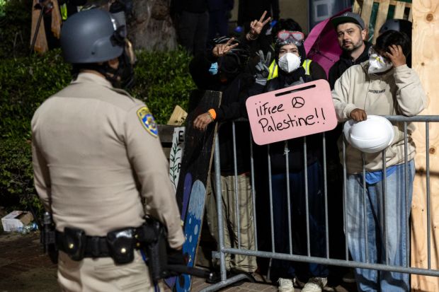A US Police officer stands guard as a demonstrator holds a placard reading "Free Palestine" at a pro-Palestinian encampment set up on on the campus of the University of California Los Angeles (UCLA), after clashes erupted in Los Angeles on May 1, 2024. Clashes broke out on May 1, 2024 around pro-Palestinian demonstrations at the University of California, Los Angeles, as universities around the United States struggle to contain similar protests on dozens of campuses. (Photo by ETIENNE LAURENT / AFP) (Photo by ETIENNE LAURENT/AFP via Getty Images)