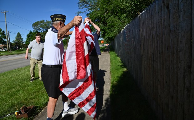 On far left is Richard J. Kennedy of Wheeling. Center, handling the new American flag is Rob Holt of Northbrook, twice past commander of the George W. Benjamin American Legion Post 791 of Northbrook, who is installing the flag at Dundee Road and Bach Street on May 25, 2024 in Northbrook. (Karie Angell Luc/Pioneer Press)