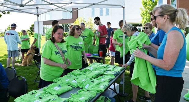 Far left, facing and laughing, Barb Freund of Northbrook is a volunteer distributing t-shirts. On far right is Liz Howard of Northbrook at the TotalLink Trot in Northbrook on May 19, 2024 at Techny Prairie Park and Fields. (Karie Angell Luc/Pioneer Press)