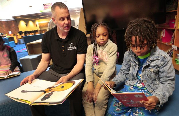 First grader teacher and School House Children's Charity fonder Brian Andreshak (left) listens to second grader Camron Jackson 7, (right) reads as Brooklyn Beal, 7, (center) waits her turn during the 2nd Annual Mother's Day Book Give Away hosted by the School House Children Charity at Glen Park Academy in Gary on May 10, 2024. (John Smierciak/Post-Tribune)