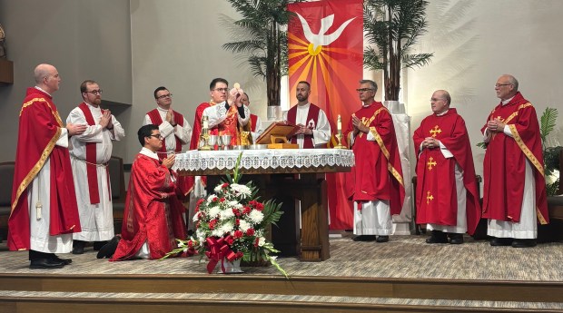 The Rev. Timothy Berryhill, center, lifts the host as part of Communion during an early morning Mass at St. George Parish in Tinley Park. It was the first Mass he celebrated after being ordained as a priest a day earlier. (Olivia Berryhill)