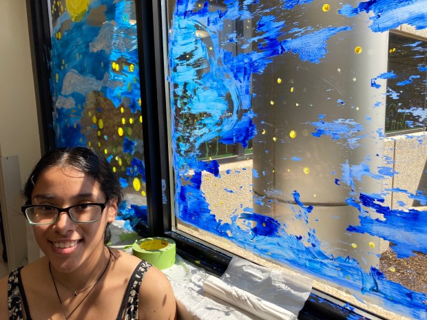 Faith Aparicio, a senior at Bremen High School in Midlothian, stands next to art she painted on a window Wednesday, May 1, at Advocate South Suburban Hospital in Hazel Crest. Some of the paint started flaking off of her original image, so she altered it and channeled famous painter Bob Ross, calling it a "happy mistake." (Paul Eisenberg/Daily Southtown)