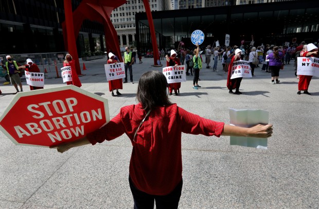 Anti-abortion activist Eileen Steffel of Glenview, back to camera, faces a row of pointing pro-choice "handmaids" as several dozen abortion activists and supporters rally during a "Bans Off My Body"protest at the Federal Plaza in Chicago, on Sept. 10, 2021. (Antonio Perez/Chicago Tribune)