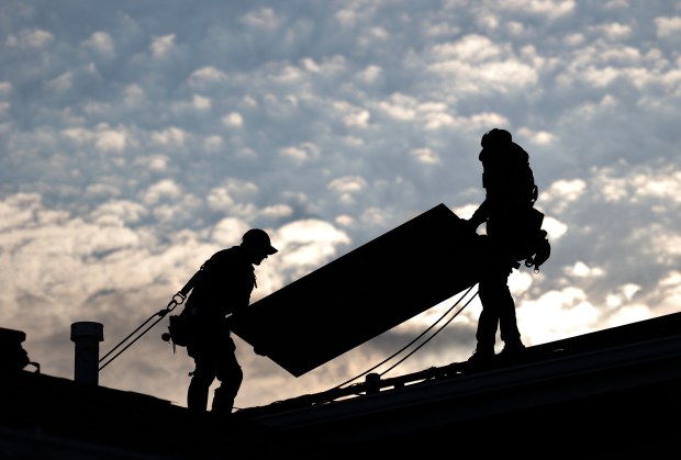 Jared Salvatore, left, and Garrison Riegel, of Celestar Solar, carry a solar panel onto a roof in Schaumburg on Nov. 30, 2023. (Trent Sprague/Chicago Tribune)