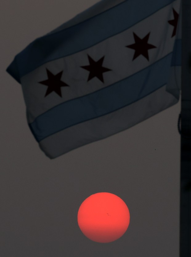 A Chicago flag waves in front of the setting sun, muted by wildfire smoke from Canada, at DePaul College Prep, June 28, 2023. (John J. Kim/Chicago Tribune)