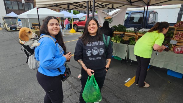 Viviana Alba of Aurora, left, and her partner Christina Garcia brought their dog Panini to the opening of the Aurora Farmers Market for the season on Saturday. (David Sharos / For The Beacon-News)