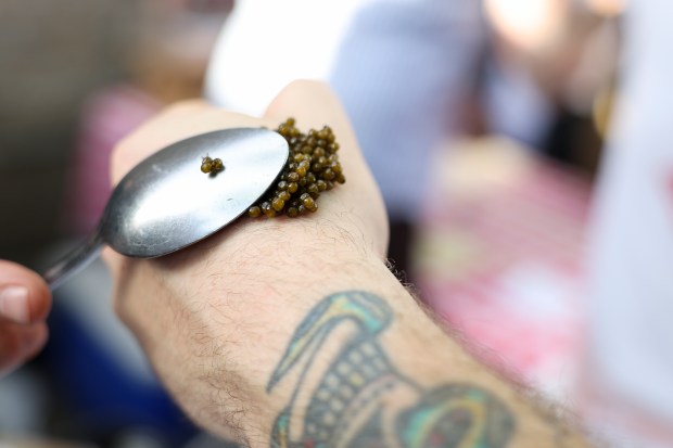 Le Bouchon chef and owner Oliver Poilevey puts caviar on the hand of Sportsman's Club general manager DJ Dodd during a Sunday BBQ on the patio of Sportsman's Club in Ukrainian Village on June 2, 2024. (Eileen T. Meslar/Chicago Tribune)