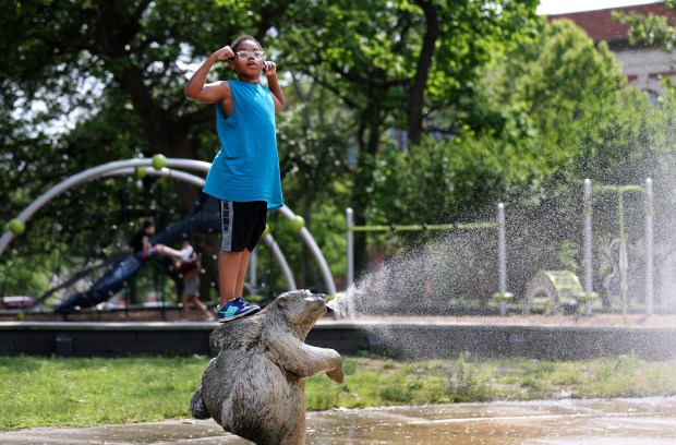 Jacaree Hughes, 9, stands atop a sprinkler while cooling off in Chicago's Douglass Park on June 13, 2024. (Chris Sweda/Chicago Tribune)