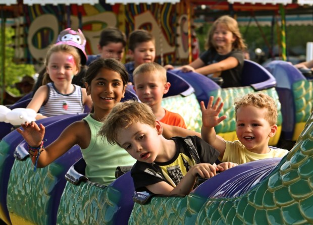 In the front row on far right, on the dragon roller coaster ride are the Woodmore siblings from Lake Zurich, (left) Rory, 4, and (waving hand) Flynn, 2, at the Friday opener of the Historic Downtown Long Grove Strawberry Fest on June 21, 2024. (Karie Angell Luc/Lake County News-Sun)