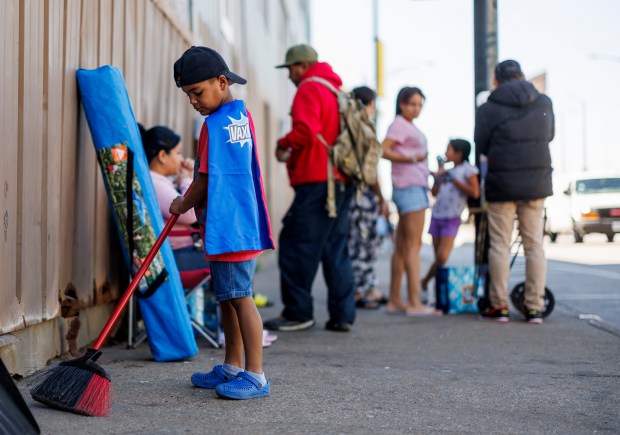 Sebastian Leal, 6, from Venezuela wears a cape while sweeping the ground outside a migrant shelter on the Lower West Side on June 12, 2024 in Chicago. The city recently announced it would begin migrant shelter evictions for family's with school aged children. (Armando L. Sanchez/Chicago Tribune)