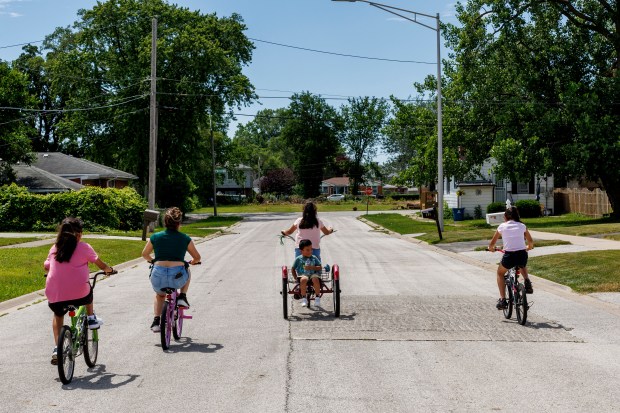 A family bikes through a street on June 26, 2024, in Phoenix, Illinois. (Armando L. Sanchez/Chicago Tribune)