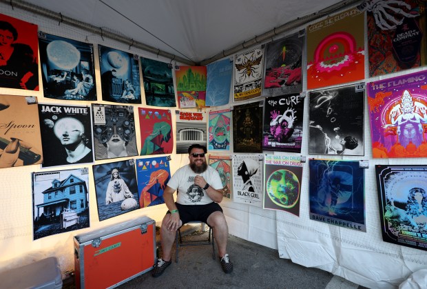 Brayn Durco sits in his friend Chris Everhart's booth at the Flatstock poster fair during Pitchfork Music Festival at Union Park Friday, July 19, 2024, in Chicago. (John J. Kim/Chicago Tribune)