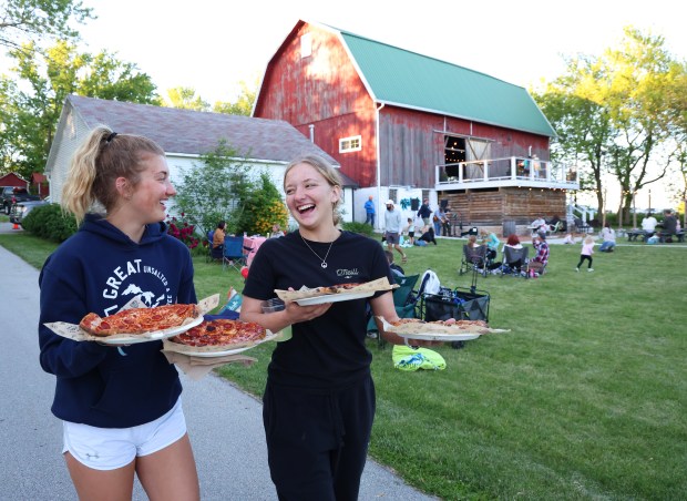 Ashleigh McCarthy, 19, left, and her sister, Calleigh McCarthy, 16, carry pizzas to their family during Farm Pizza night at Mapleton Barn on May 30, 2024, in Oconomowoc, Wisconsin. (Stacey Wescott/Chicago Tribune)