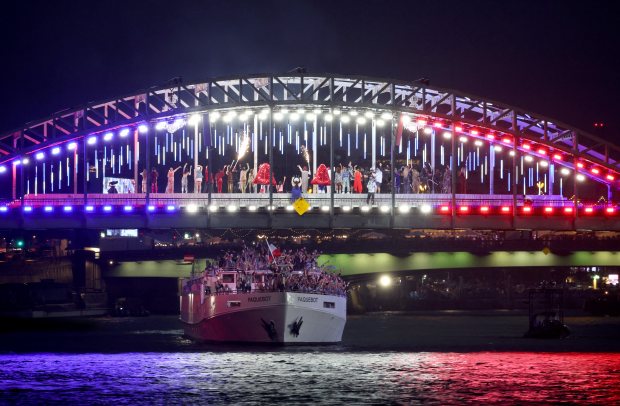 Team France passes under an illuminated on a bridge over the Seine river as dancers perform for the Parade of Athletes during the opening ceremony of the 2024 Summer Olympics on July 26, 2024, in Paris. (Brian Cassella/Chicago Tribune)